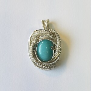 May include: A silver wire wrapped pendant featuring a light blue oval gemstone.