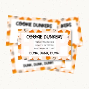 May include: A rectangular card with a white center and a border featuring orange, yellow, and white candy corn icons and black triangles. The text reads: COOKIE DUNKERS, FIRST YOU TAKE A COOKIE, DUNK IT IN THE TOPPING, NOW ENJOY YOUR COOKIE, DUNK, DUNK, DUNK!