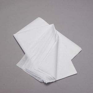 Puede incluir: Una pila de papel de seda blanco doblado sobre un fondo gris. El papel está en capas, con pliegues y arrugas visibles. Los bordes son limpios y nítidos, lo que sugiere un producto nuevo.