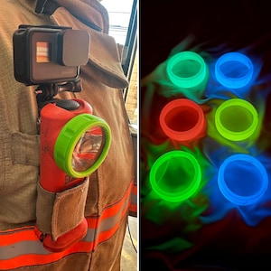 Puede incluir: Una linterna roja con un bisel verde está sujeta a la chaqueta de un bombero, junto a una cámara GoPro. La imagen también muestra seis objetos circulares brillantes en tonos verdes, rojos y azules, posiblemente relacionados con la linterna.