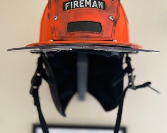 May include: An orange firefighter helmet with a black visor and a black strap. The helmet has a white label that reads "PROBATIONARY FIREMAN".
