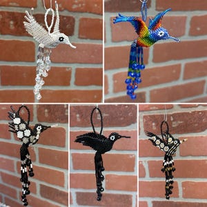 May include: Five beaded hummingbird ornaments in various colors. The hummingbirds are made of beads and have long beaks and dangling bead tails. The colors include white, rainbow, black, and black and white.