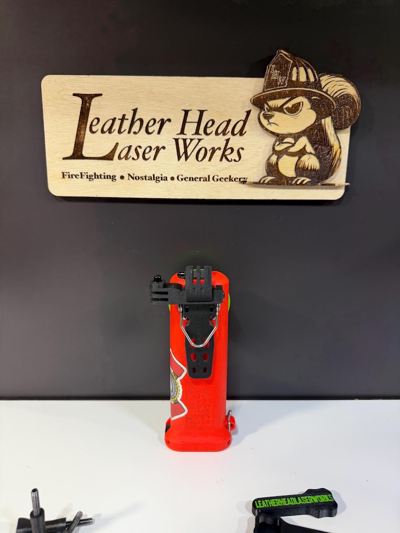 May include: A red fire extinguisher with a black mounting bracket and a decorative emblem. The image also features a wooden sign with the text "Leather Head Laser Works" and a cartoon squirrel wearing a firefighter's helmet.