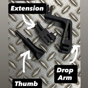 May include: Black metal extension, drop arm, and thumb screw components. The parts are arranged on a diamond plate surface. A cartoon squirrel wearing a firefighter's hat is in the upper left corner. The words "Extension", "Drop Arm", and "Thumb Screw" are labeled.