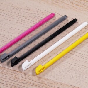 May include: Five stylus pens in different colours: pink, grey, black, white and yellow. The pens are all the same size and shape, with a pointed tip.