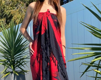 Op de afbeelding: Een rode en zwarte sarong met een bloemenprint en franjes. De sarong is om de taille gebonden en wordt als jurk gedragen.