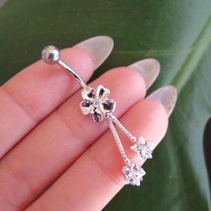 May include: Silver belly button ring with a dangling flower charm and three clear crystal stones.