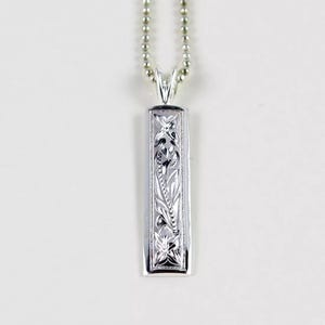 May include: A silver necklace with a rectangular pendant featuring an intricate floral design.