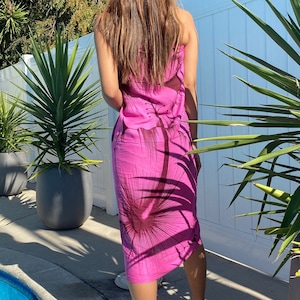 Op de afbeelding: Een roze sarong met een bruine bloemenprint. De sarong is om de taille gebonden en valt tot aan de knie&euml;n. De persoon draagt ​​slippers.