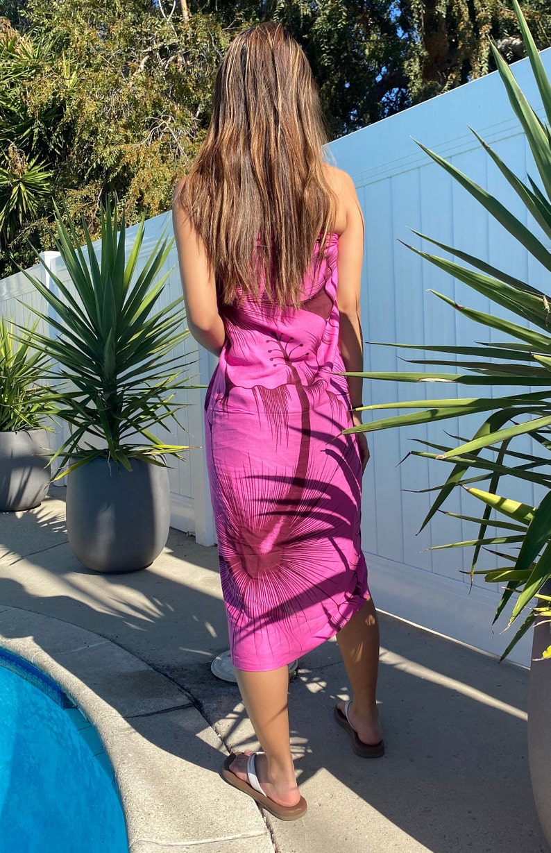 Op de afbeelding: Een roze sarong met een bruine bloemenprint. De sarong is om de taille gebonden en valt tot aan de knie&euml;n. De persoon draagt ​​slippers.