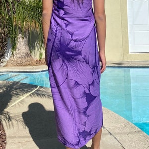 Op de afbeelding: Een paarse sarong met een groot hibiscusbloemmotief. De sarong is om de taille gebonden en valt tot aan de enkels.