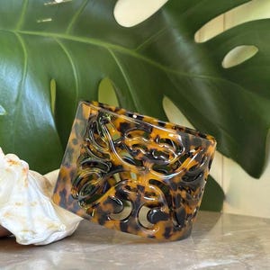 Puede incluir: Una taza de cerámica blanca con asa negra y el texto "But First, Coffee" en negro, con una fuente de estilo manuscrito. La taza está sobre una superficie blanca.