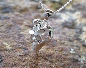 Puede incluir: Un collar de plata con un colgante en forma de corazón que presenta un delicado diseño floral. El colgante tiene una pequeña piedra transparente en el centro de la flor.