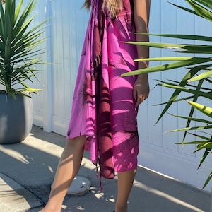 Op de afbeelding: Een roze en bruine sarong met een bloemenprint. De sarong is om de taille gebonden en heeft een franje aan de onderkant.