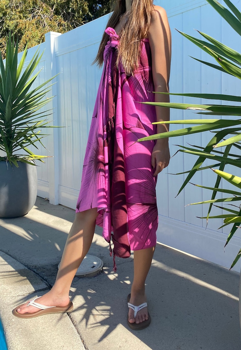 Op de afbeelding: Een roze en bruine sarong met een bloemenprint. De sarong is om de taille gebonden en heeft een franje aan de onderkant.