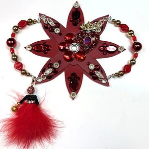 Peut inclure: Un serre-tête en forme d'étoile bordeaux, orné de pierres précieuses rouges, d'accents argentés et d'un bijou central en forme de cœur avec une couronne. Une chaîne de perles et une poupée avec une jupe en plumes rouges complètent le design.