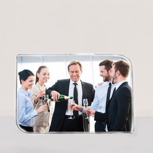 May include: A group of five people in business attire are celebrating with champagne. The person in the center is pouring champagne into a glass held by the person to their right. The people are smiling and looking at each other.