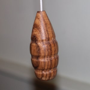May include: A wooden light pull with a brown and dark brown wood grain pattern. The pull is shaped like a teardrop and has a smooth, rounded surface.