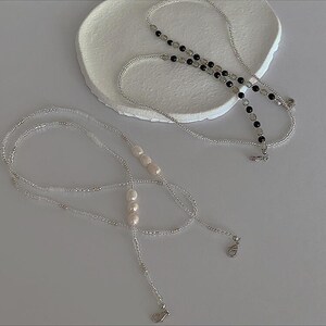 May include: Two beaded necklaces, one with white pearls and one with black and clear beads. Both necklaces have silver clasps.