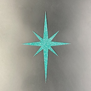 Może przedstawiać: Ośmiopromienna gwiazda z turkusowego brokatu. Gwiazda jest wycięta z papieru i znajduje się na szarym tle.