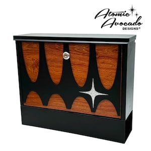 Może przedstawiać: Czarna i brązowa skrzynka pocztowa w stylu mid-century modern z wzorem gwiazdy i dziurką od klucza. Skrzynka pocztowa jest wykonana z metalu i ma wykończenie imitujące drewno. "Atomic Avocado Designs" jest nadrukowane na górze skrzynki pocztowej.