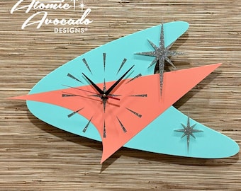 May include: A turquoise and coral colored mid-century modern style clock with silver glitter accents. The clock features a starburst design and the text "Atomic Avocado Designs".