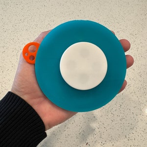 May include: A teal blue silicone sink stopper with a white center and an orange handle with three holes.