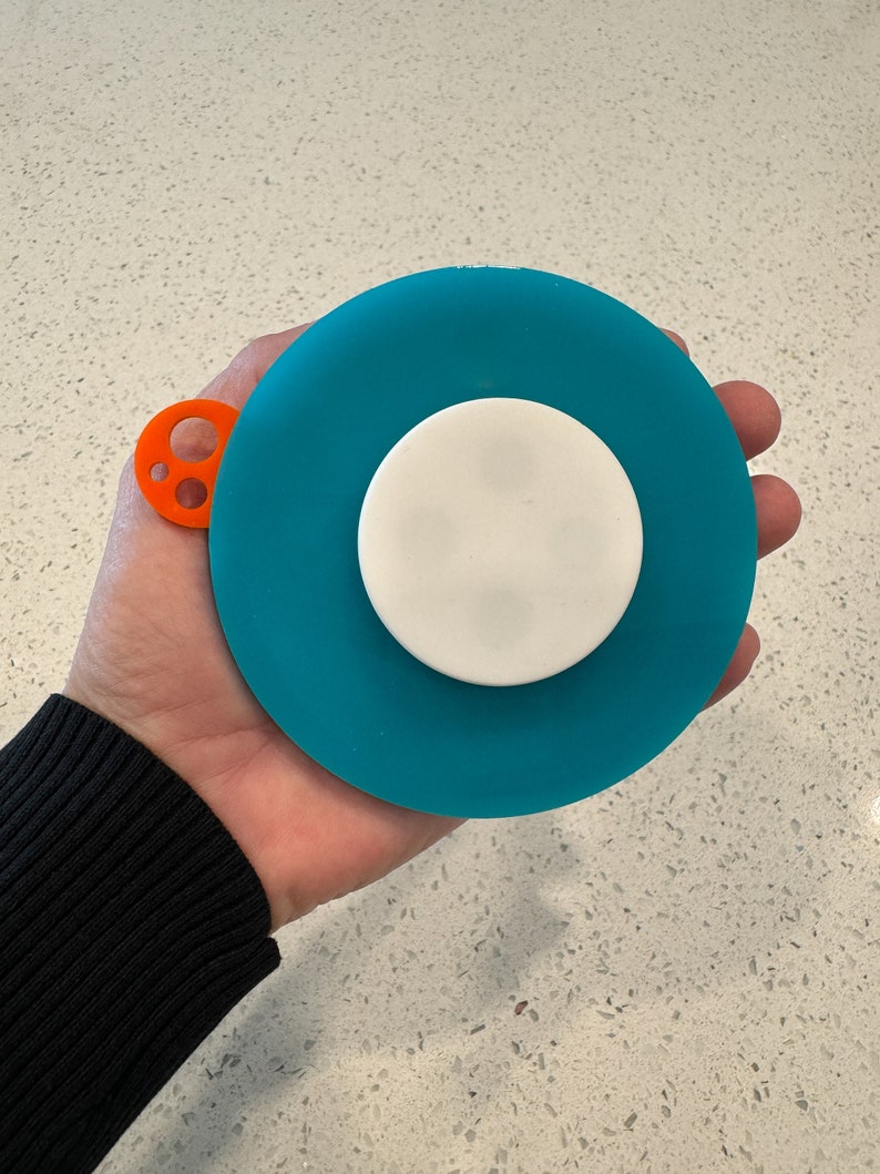 May include: A teal blue silicone sink stopper with a white center and an orange handle with three holes.
