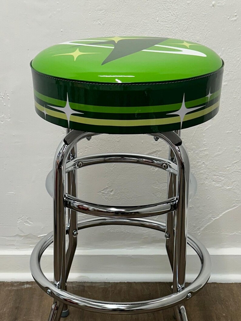 Puede incluir: Un taburete de bar verde y blanco con base cromada. El asiento est&aacute; tapizado en vinilo verde con un dise&ntilde;o de estrella blanca.