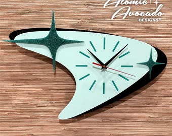 May include: A turquoise and black atomic-style clock with a boomerang-shaped face and two glitter stars. The clock face has a red hour hand, a black minute hand, and teal hour markers.