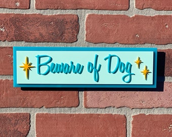 May include: A blue and white sign with the text "Beware of Dog" in a turquoise blue font. The sign has two yellow stars on either side of the text.