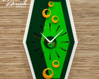 May include: A green and white atomic-style clock with a white face and black hands. The clock has a green background with a smaller green circle in the center. There are five yellow circles around the clock face.