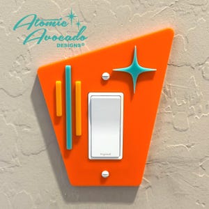 Könnte beinhalten: Orangener Lichtschalter-Abdeckung mit geometrischem Design und einem türkisfarbenen Stern. Die Abdeckung hat zwei orange und türkisfarbene Streifen und den Text "Legrand" auf dem Schalter.