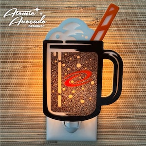 May include: A night light shaped like a mug of root beer, featuring a black outline and a glittery brown interior. The mug has a handle and a straw. The top has a blue and white foam design. The text "Atomic Avocado Designs" is in the upper left corner.