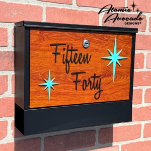 May include: A black mailbox with a woodgrain finish and a metal door. The mailbox has a turquoise star design and the text "Fifteen Forty" on the front.