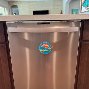 May include: A stainless steel dishwasher with a silver handle and a blue and orange "Clean" magnet on the front.
