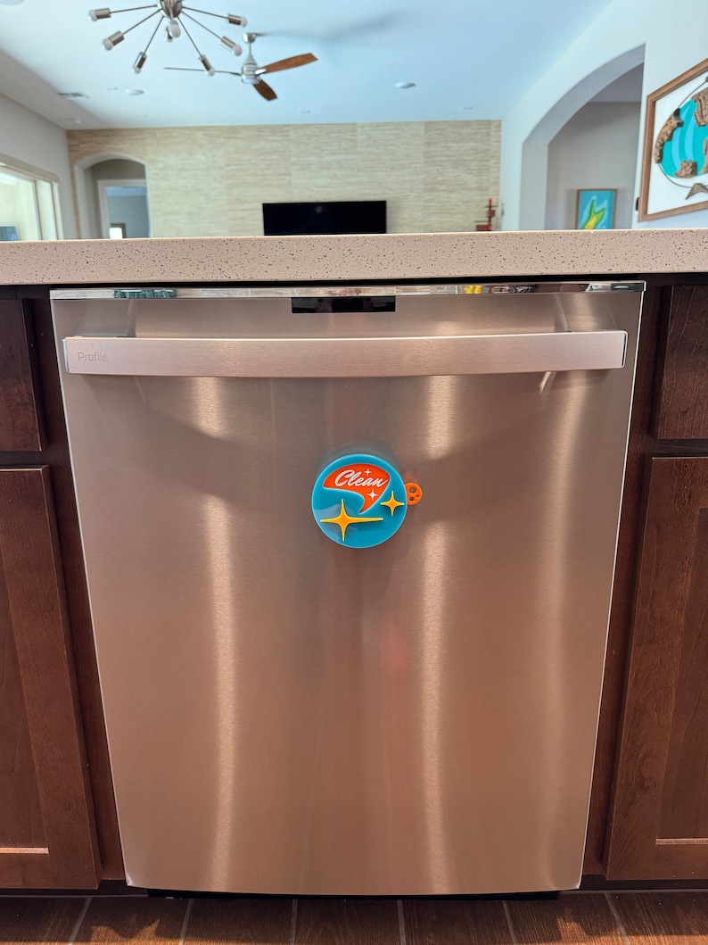 May include: A stainless steel dishwasher with a silver handle and a blue and orange "Clean" magnet on the front.