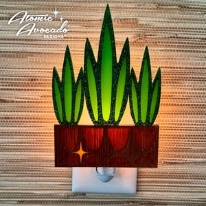May include: A green and brown night light shaped like a potted plant with the text "Atomic Avocado Designs" on the top.