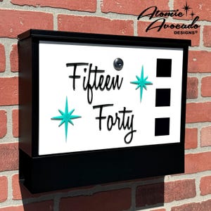 May include: Black mailbox with a white front panel. The front panel has a turquoise starburst design and the text "Fifteen Forty" in black cursive font. There are three rectangular slots on the right side of the panel.