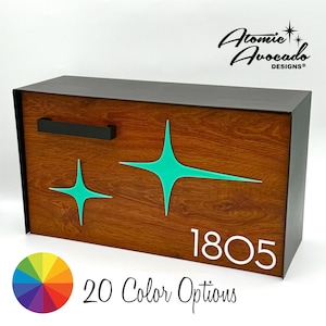 Puede incluir: Un buzón de madera con un marco de metal negro y un diseño de estrella estrellada turquesa. El buzón tiene una manija negra y el número 1805 se muestra en la parte delantera. El buzón está disponible en 20 opciones de color.