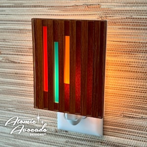 Könnte beinhalten: Ein Nachtlicht aus Holz mit einem Stecker. Das Licht hat ein geometrisches Design mit roten, grünen und orangefarbenen Akzenten.