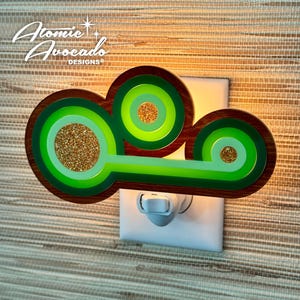 May include: A green and brown night light shaped like a cloud with a gold glitter accent. The night light plugs into a standard outlet.