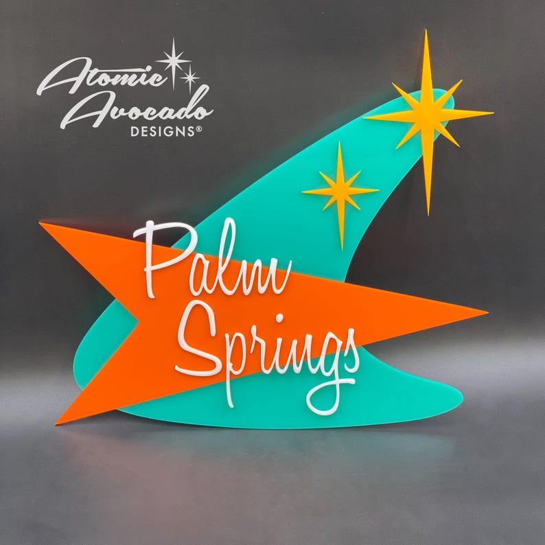 K&ouml;nnte beinhalten: Ein retro-stiles Schild in T&uuml;rkisblau und Orange mit dem Text "Palm Springs" in wei&szlig;er, kursiv geschriebener Schrift. Das Schild zeigt zwei gelbe Sterne mit wei&szlig;em Rand.
