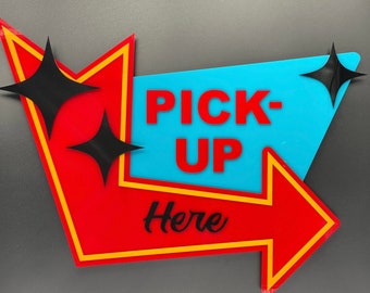 May include: A red and yellow arrow sign with a blue centre panel that says "PICK-UP Here". The sign has two black star-shaped accents.