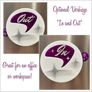 May include: Two white round magnetic signs with a purple, abstract, boomerang-shaped design. One sign says "Out" and the other says "In". Both signs have silver glitter stars.