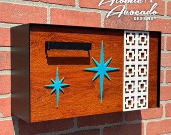 Puede incluir: Un buzón de madera con marco negro y un diseño de estrella estrellada turquesa. El buzón tiene una manija de metal negro y un patrón geométrico blanco en el lado derecho. El texto "Atomic Avocado Designs" está impreso en blanco en la parte superior del buzón.