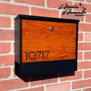Puede incluir: Un buzón negro con diseño de veta de madera y el número de casa 10717. El buzón tiene un marco de metal negro y un panel de veta de madera con una solapa de metal negro.