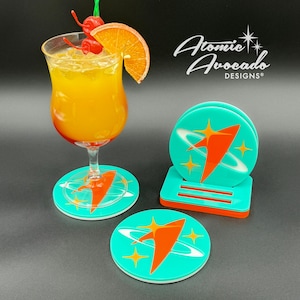 May include: Set of four turquoise coasters with a white and orange retro space-age design. The coasters feature a stylized rocket ship with a white outline and a red interior. The coasters are arranged in a stack with a red base. The text "Atomic Avocado Designs" is visible in the background.