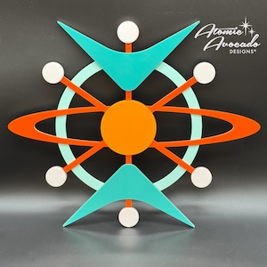 May include: A mid-century modern wall art piece featuring a stylised atom design with a bright orange centre, turquoise blue wings, and a red ring around the centre. The piece is made of wood and has a minimalist design.