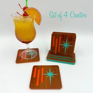 May include: Set of four coasters with a mid-century modern design. The coasters are made of wood with a light brown finish and have a teal starburst design with orange accents. The coasters are shown in a stack with a teal base.